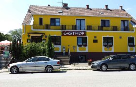 Gelbes Gebäude mit der Aufschrift 'Gasthof', Autos davor geparkt.