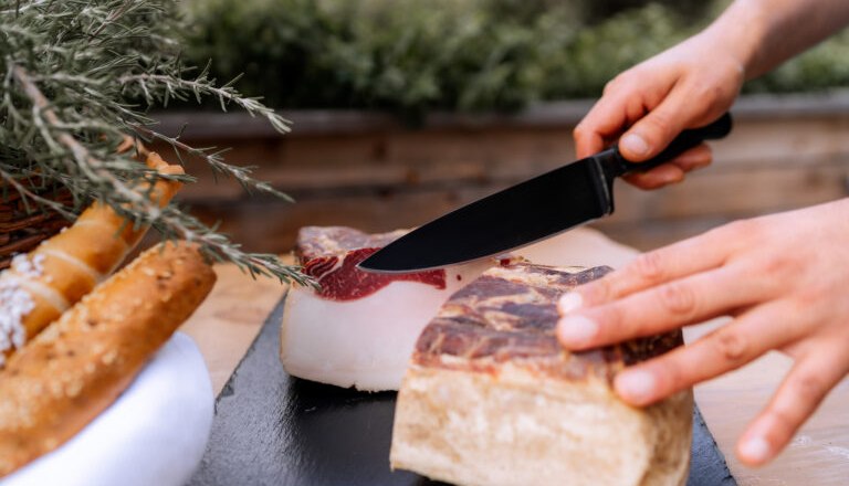 Person schneidet Speck auf einem Holzbrett.