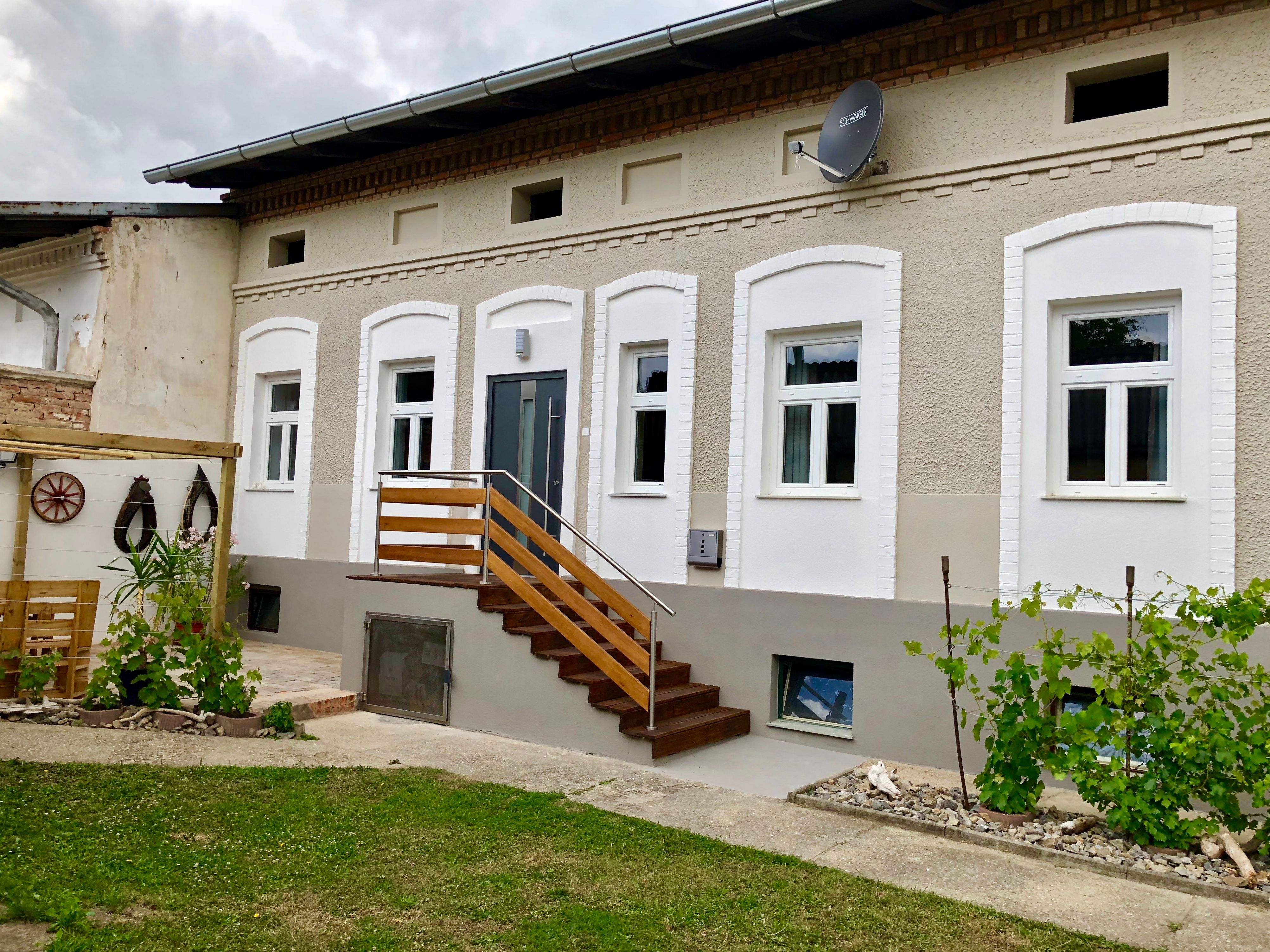 Ein renoviertes Haus mit weißen Fenstern und einer Holztreppe, umgeben von einem kleinen Garten mit Pflanzen.