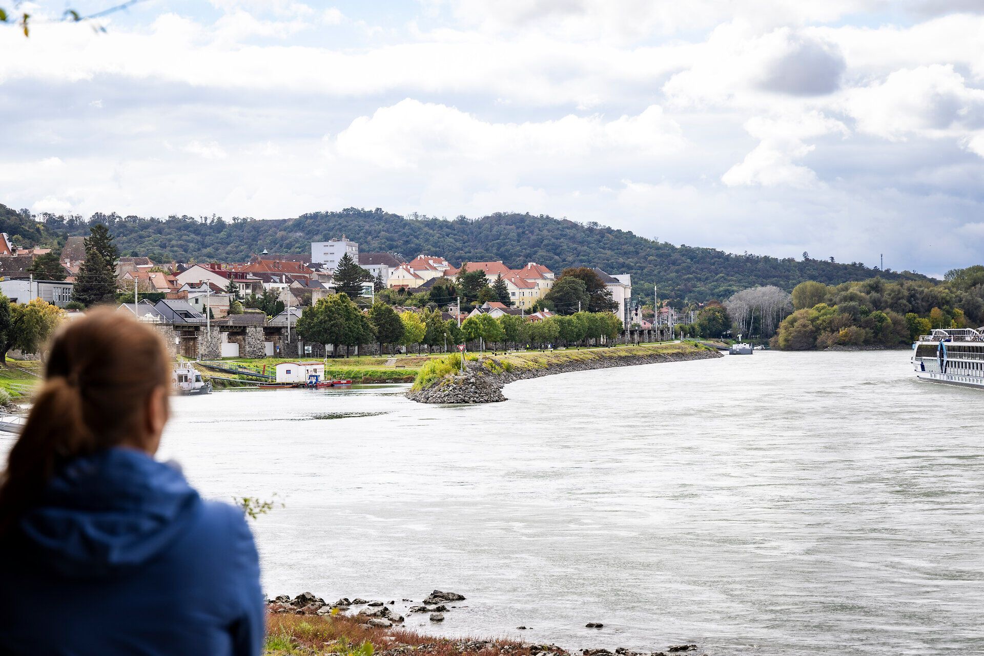 Eine Frau blickt auf die Donau und die Häuser von Hainburg am Donauufer.