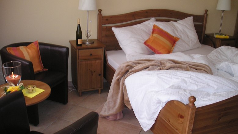 Gem&uuml;tliches G&auml;stezimmer mit Doppelbett, Nachttisch, Lampe, Sessel und Tisch.