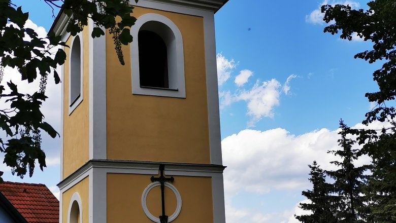 Glockenturm in Ragelsdorf vor blauem Himmel und B&auml;umen.