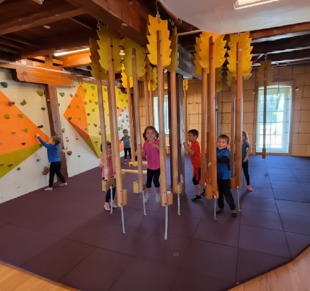 Kinder spielen in einem Indoor-Kletterraum mit Kletterwand und hängenden Elementen.