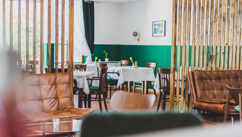 Ein stilvoll eingerichteter Gastraum mit Holzm&ouml;beln, gr&uuml;nen W&auml;nden und wei&szlig;en Tischdecken.