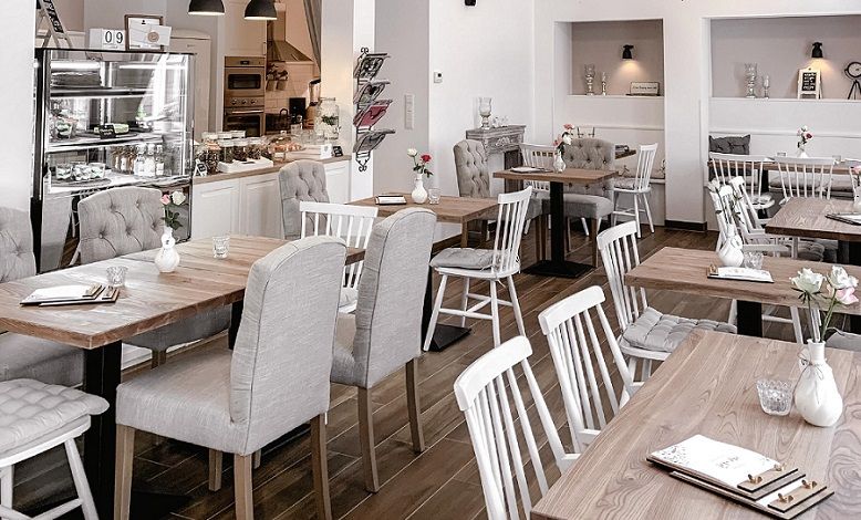 Innenansicht eines gemütlichen Cafés mit Holztischen und gepolsterten Stühlen.