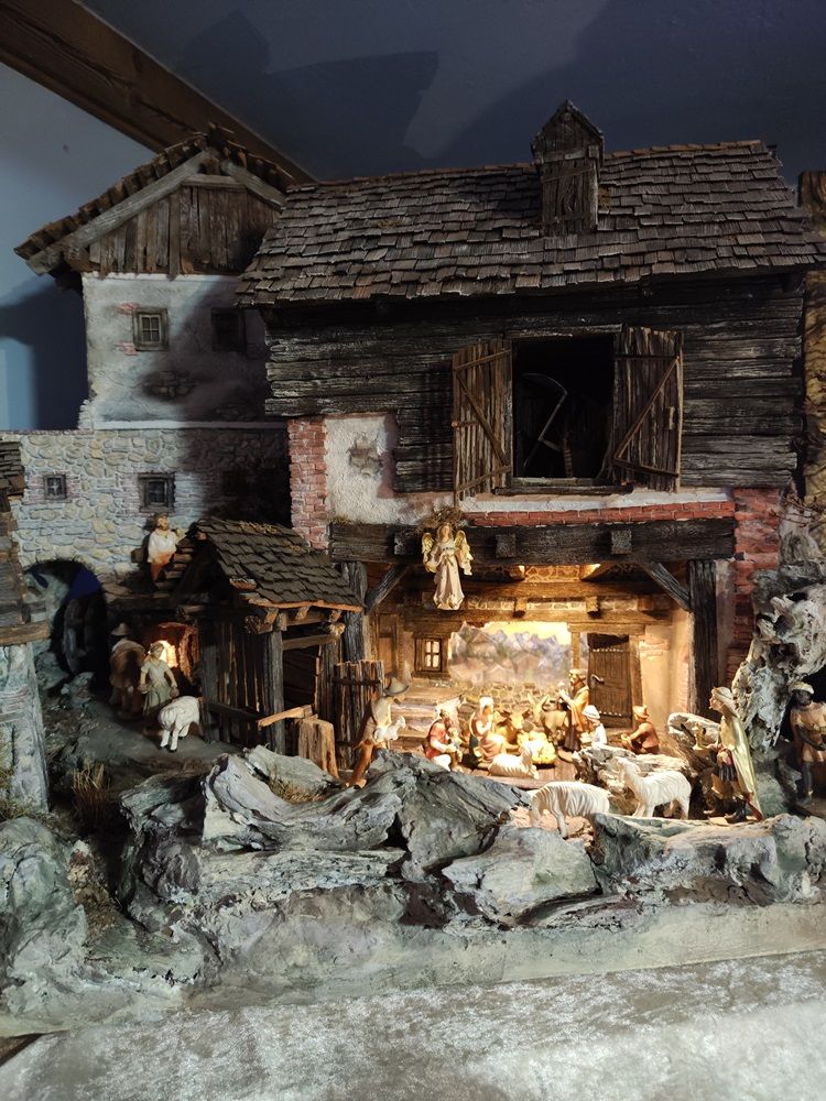 Detailreiche Krippe mit Figuren in einer rustikalen Scheune, umgeben von Schafen und Hirten.
