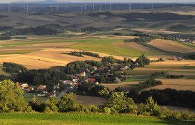 Landschaft mit Feldern, einem Dorf und Windr&auml;dern im Hintergrund.