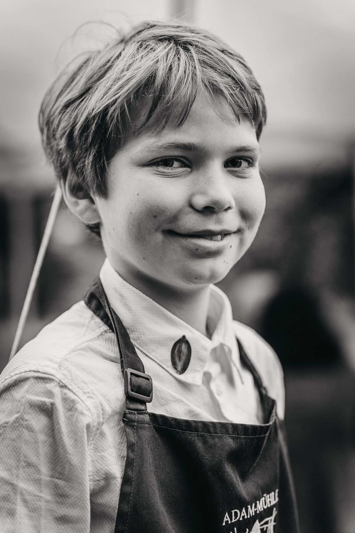 Ein Junge in einer Schürze mit der Aufschrift "Adam-Mühle" lächelt in die Kamera.