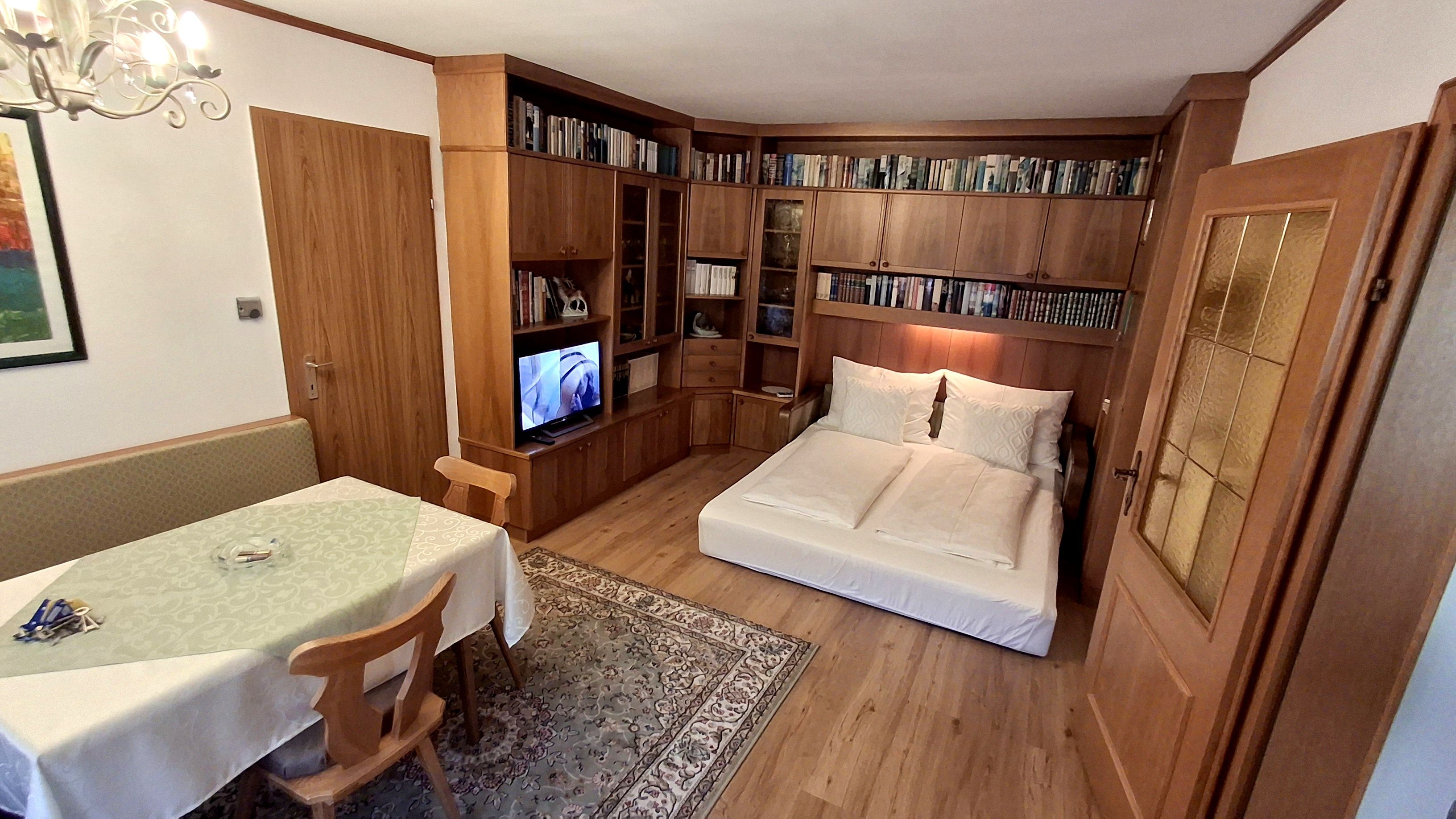 Wohnzimmer mit ausziehbarer Couch, Bücherregal, Esstisch und Fernseher.