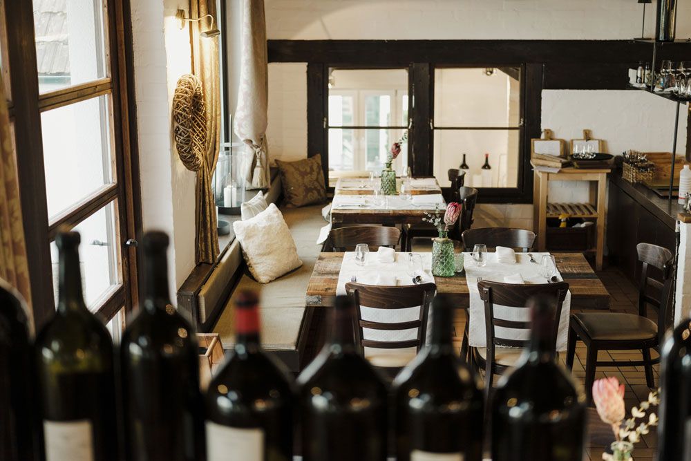 Gemütliches Restaurant mit Holztischen und Weinflaschen im Vordergrund.