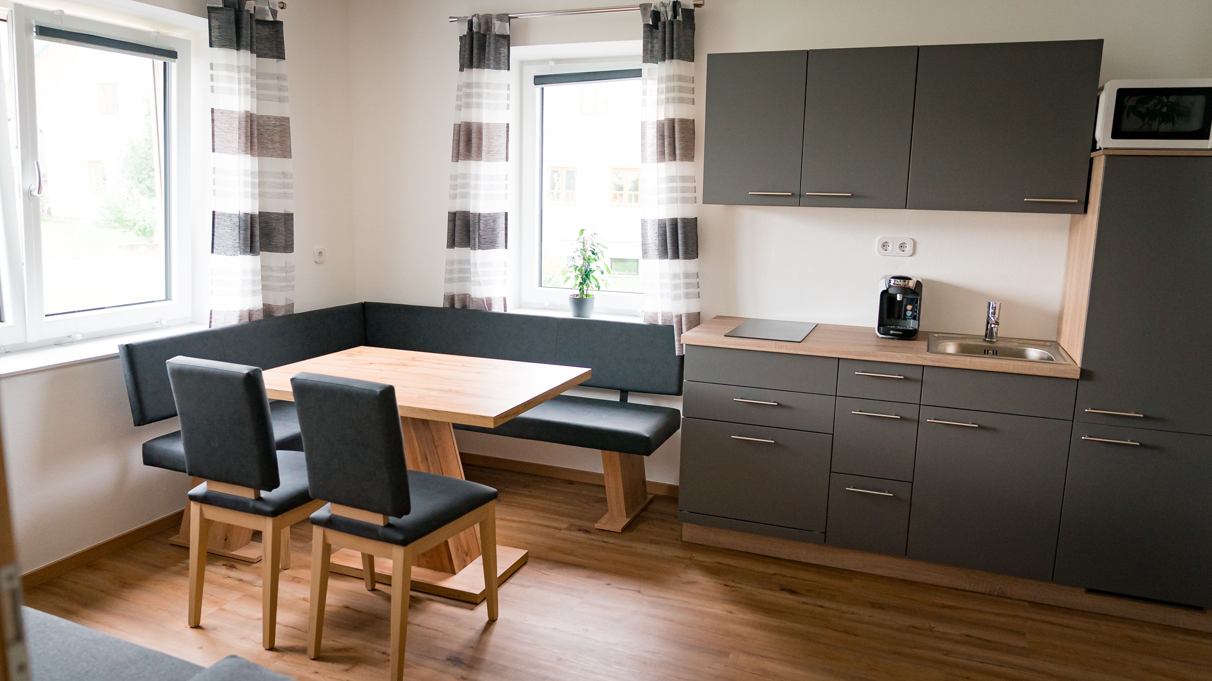 Moderne Küche mit grauen Schränken, Holztisch und Eckbank.