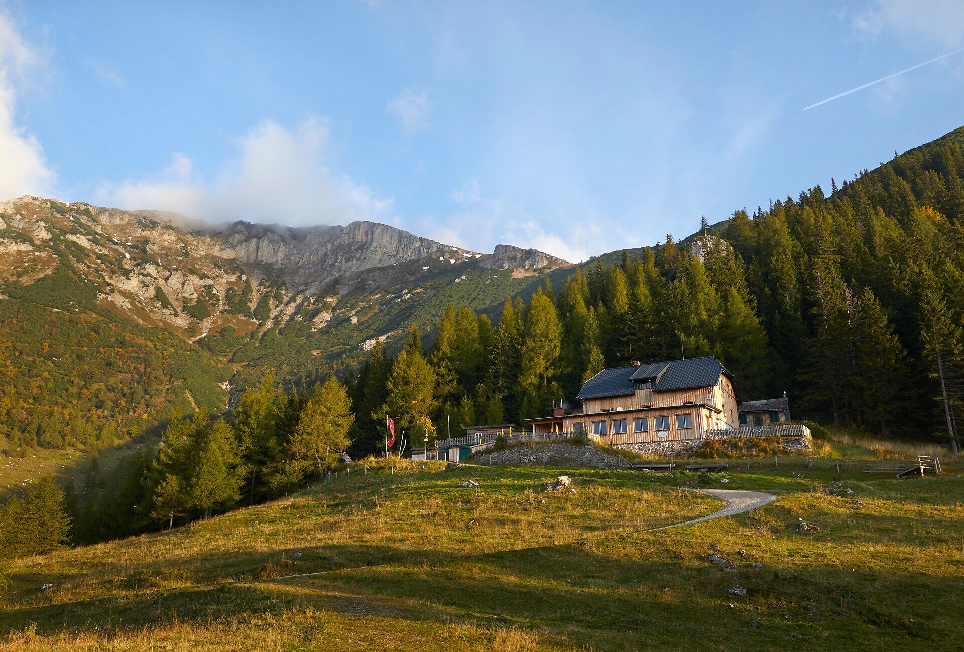 Alm- oder Berggasthof auf einer Wiese vor herbstlicher Berglandschaft.