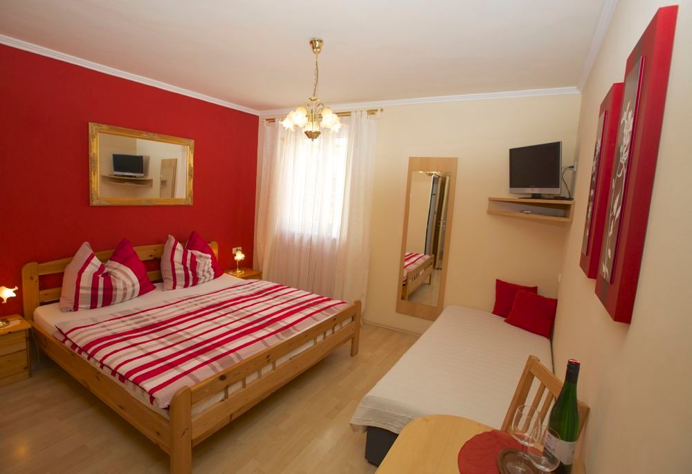 Gemütliches Zimmer mit Doppelbett, Einzelbett, roter Akzentwand und TV.