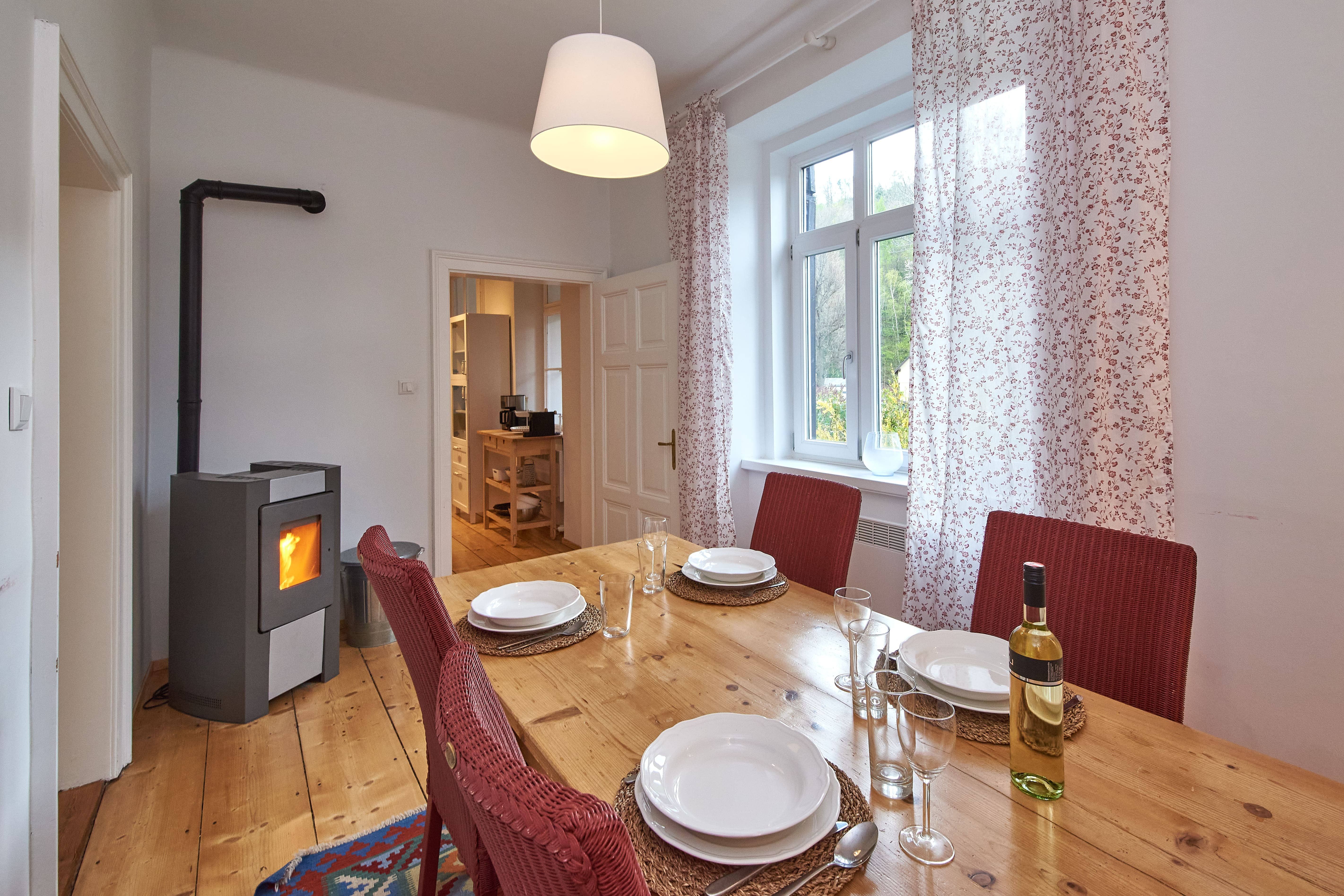 Esszimmer mit Holztisch, roten Stühlen, gedecktem Tisch und Kaminofen.