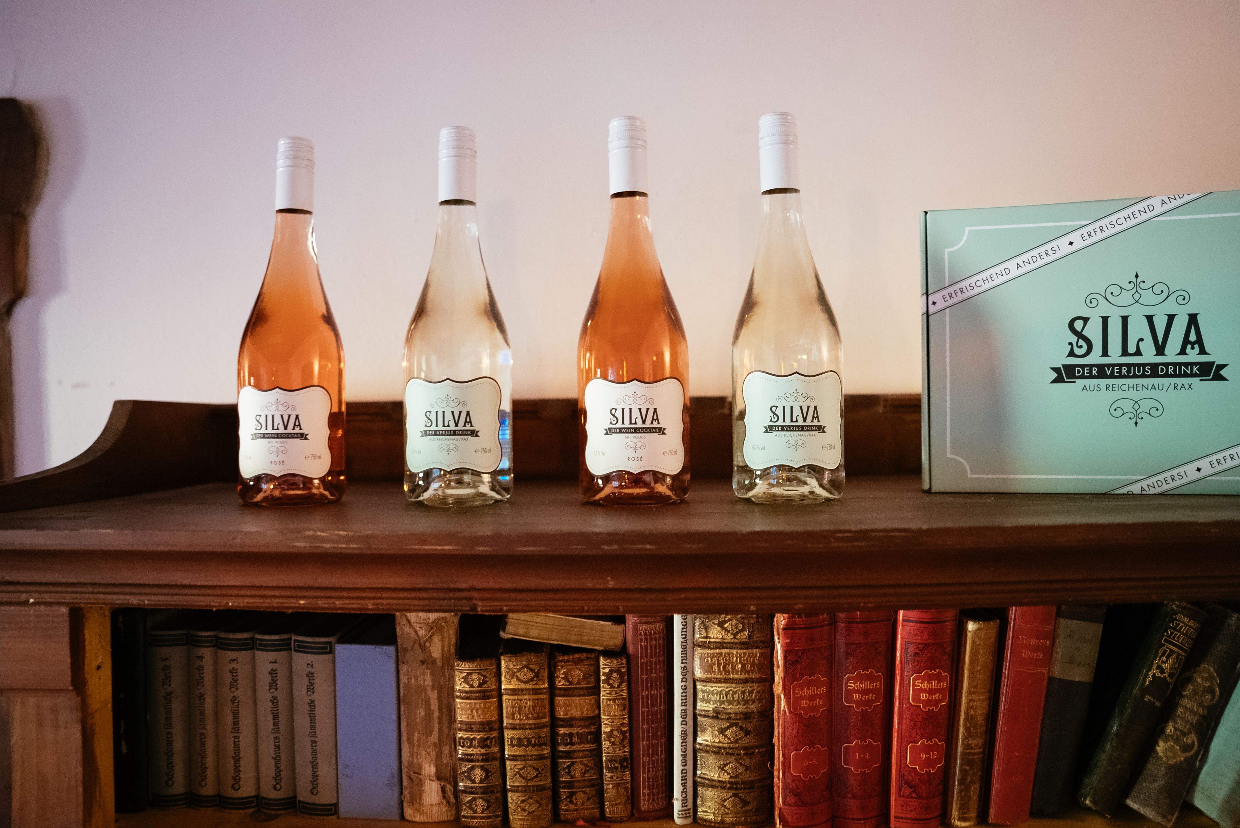 Flasche und Glas mit Silva-Verjus-Drink auf einem Betonpfeiler, unscharfe Personen im Hintergrund.