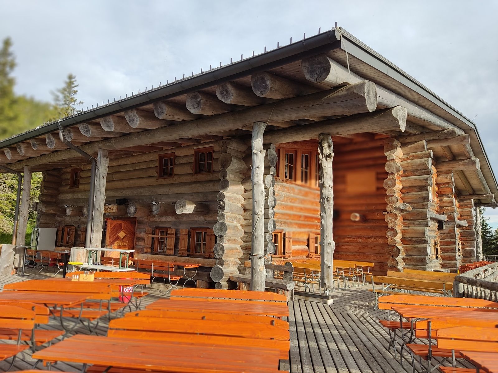Holzhütte mit Terrasse und Bänken im Freien.
