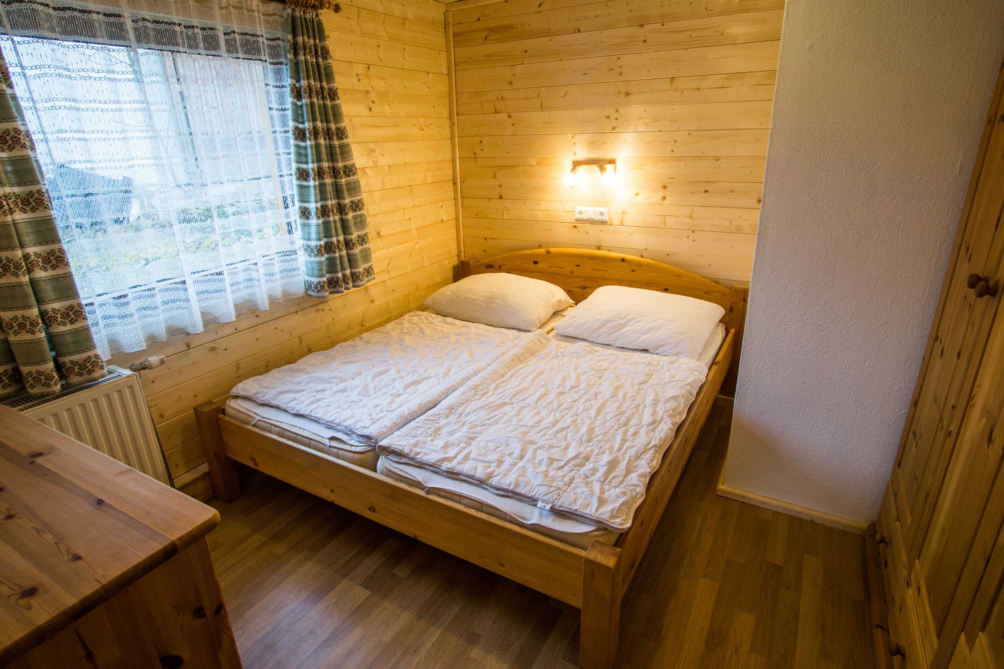 Gemütliches Schlafzimmer mit Holzwänden, Doppelbett und Fenster mit Vorhängen.