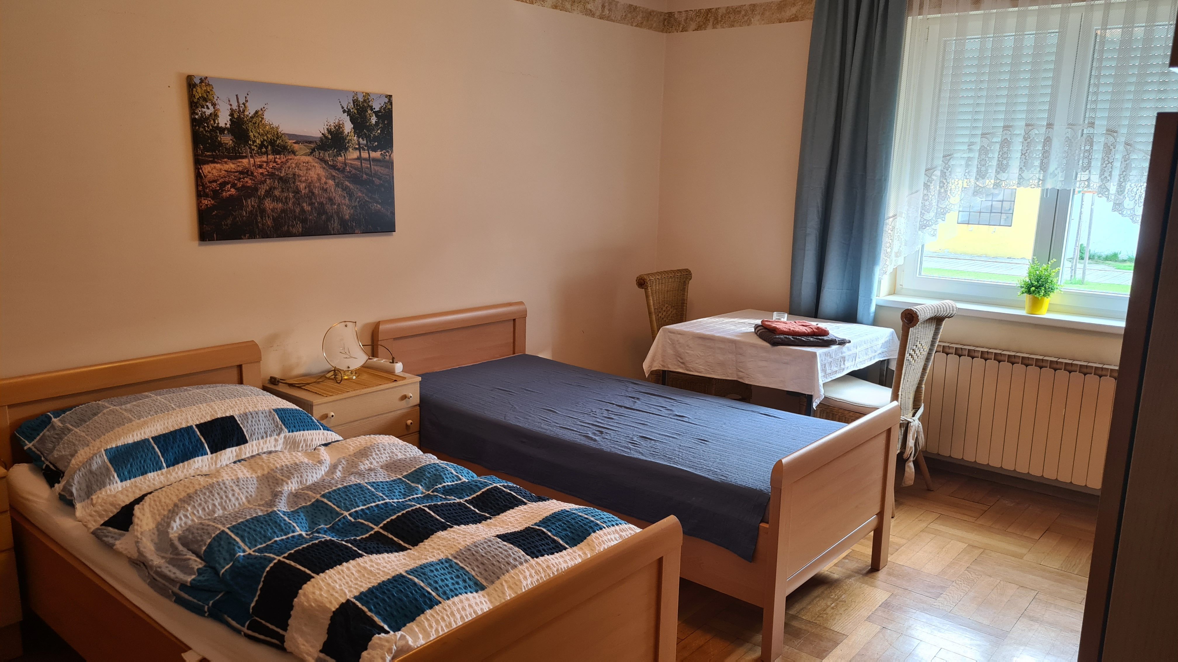 Ein einfach eingerichtetes Schlafzimmer mit zwei Einzelbetten, einem Tisch mit Stuhl und einem Fenster mit Vorhängen.