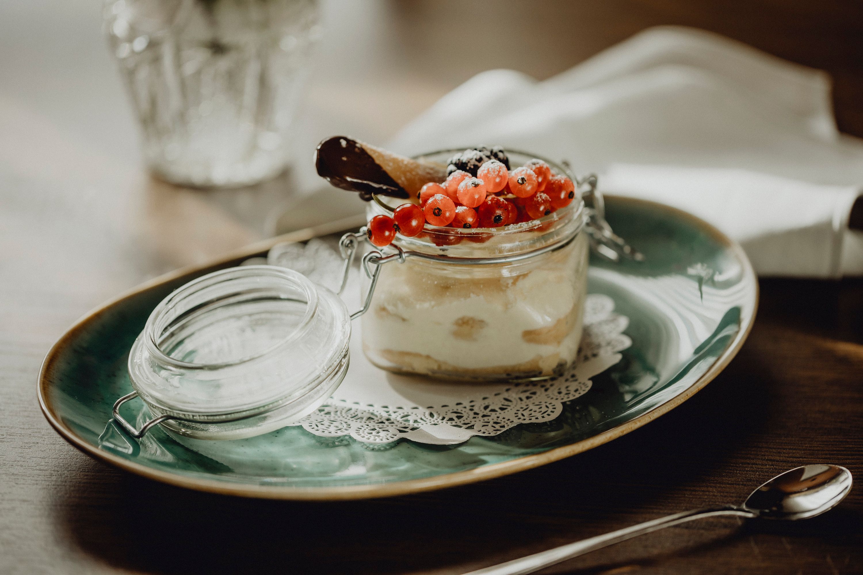 Dessert im Glas mit roten Johannisbeeren und Schokoladenkeks auf grünem Teller.