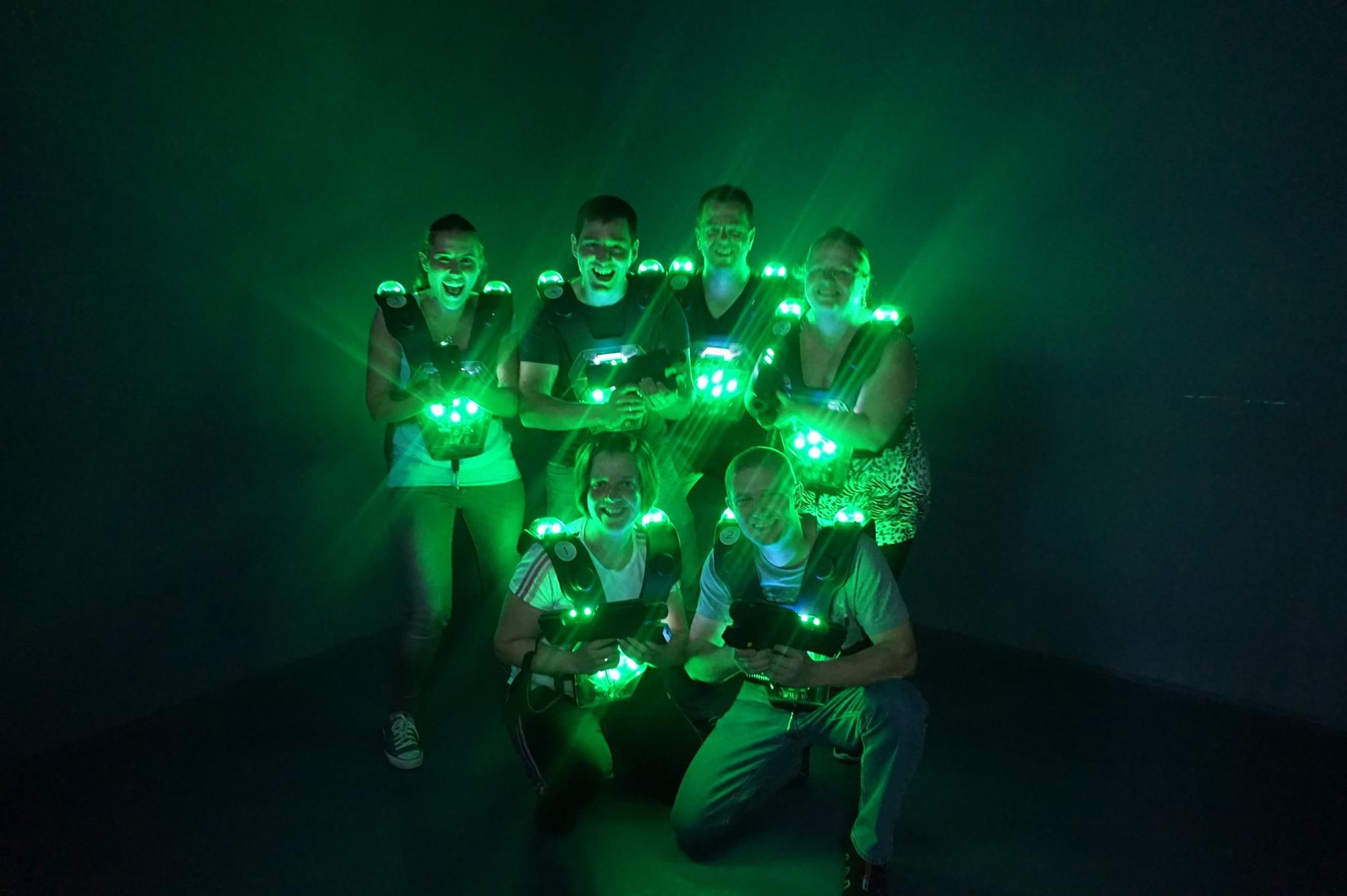 Gruppe von sechs Personen in Lasertag-Ausrüstung mit grünen Lichtern in einem dunklen Raum.