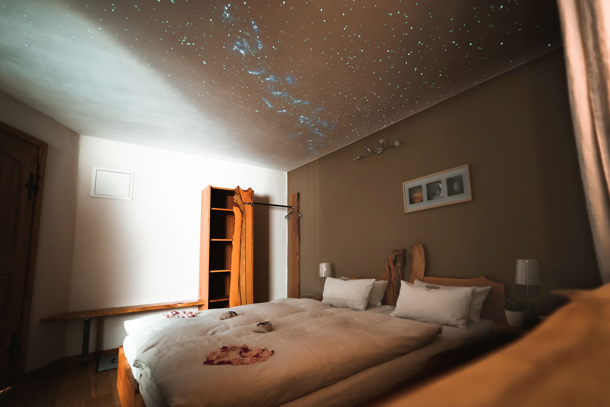 Ein gemütliches Gästezimmer mit einem Doppelbett, dekoriert mit Rosenblättern. An der Decke ist ein Sternenhimmel projiziert.