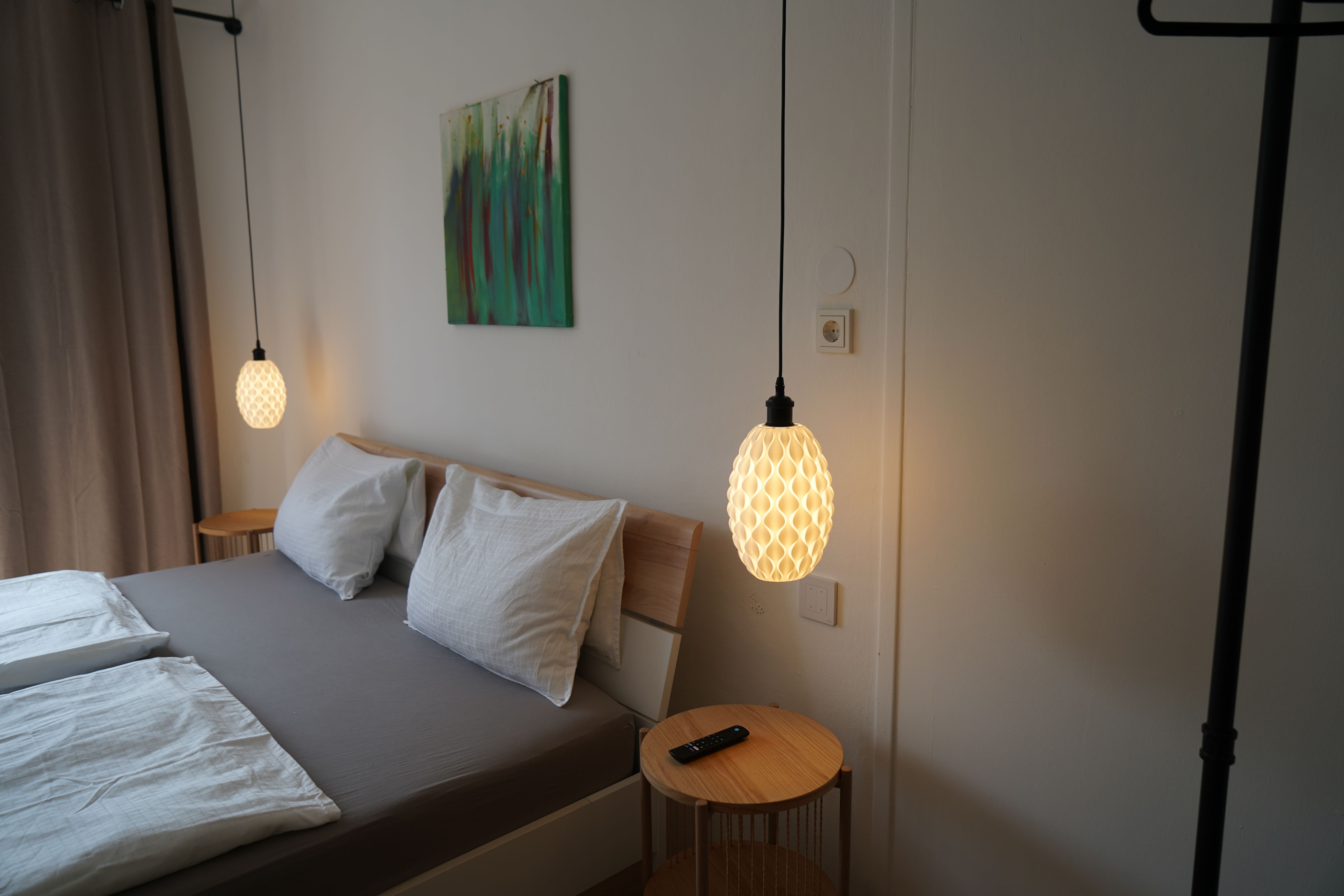 Ein modernes Schlafzimmer mit Doppelbett, zwei hängenden Lampen und einem kleinen Tisch mit Fernbedienung.