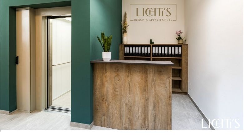 Empfangsbereich mit Holztheke, grünem Wandbereich und Aufzug.