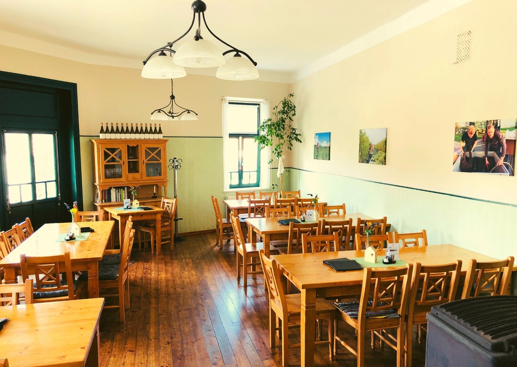 Ein gemütlicher Gastraum mit Holztischen und -stühlen, dekoriert mit Weinflaschen und Bildern an der Wand.