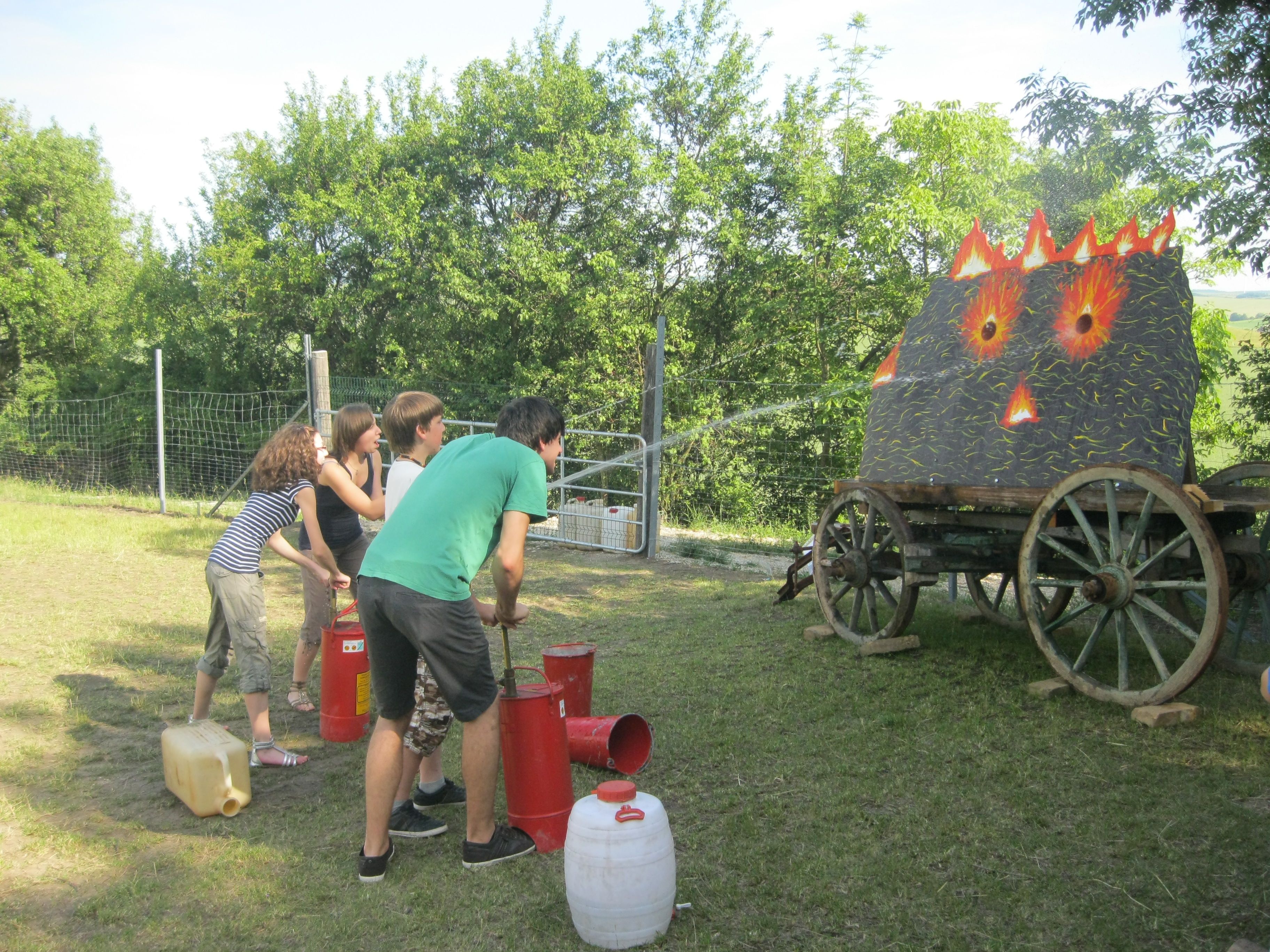 Menschen löschen ein simuliertes Feuer auf einem Wagen mit Wasserstrahlen.