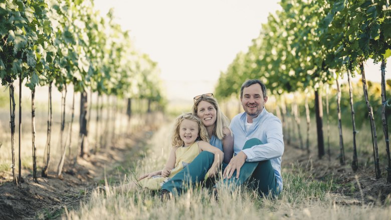 Familie sitzt zwischen Weinreben in einem Weinberg.