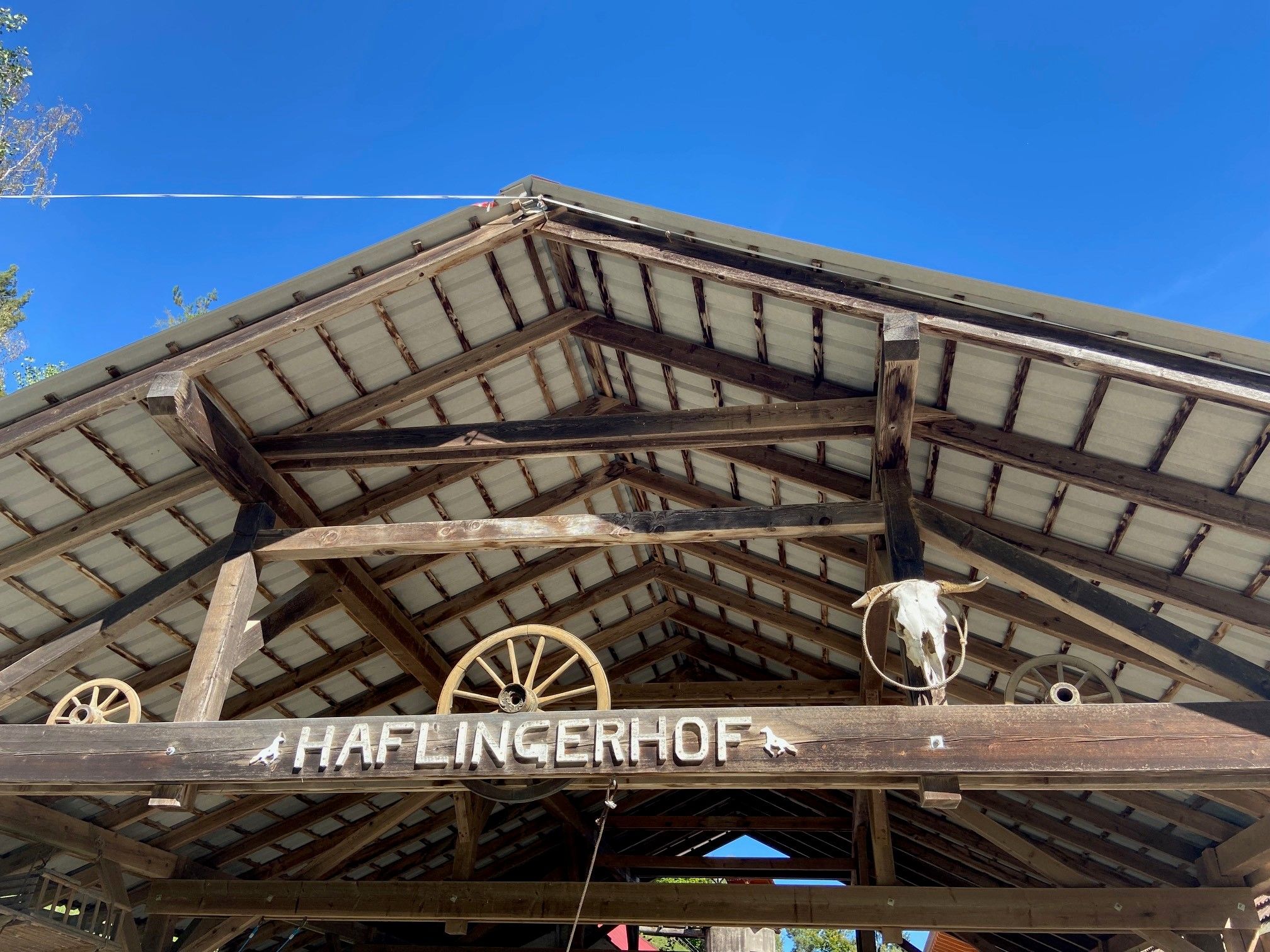 Dach eines Holzgebäudes mit Schriftzug 'Haflingerhof' und Dekorationen wie Wagenrädern und einem Tierkopf.