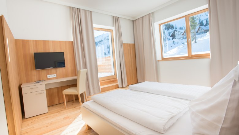 Helles Hotelzimmer mit Doppelbett, Schreibtisch und Blick auf verschneite Berge.