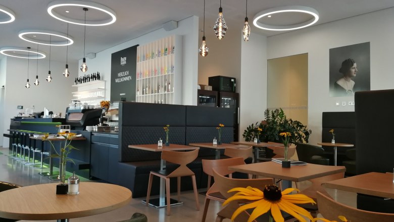 Innenansicht eines modernen Cafés mit runden Deckenleuchten, Holztischen und Blumen auf den Tischen.