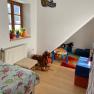 Kinderzimmer mit Bett, Spielzeug und buntem Teppich.