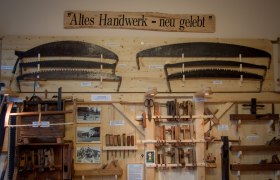 Ausstellung von alten Handwerkzeugen an einer Holzwand mit dem Schild 'Altes Handwerk - neu gelebt'.