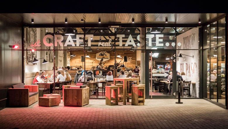 Außenansicht eines Restaurants mit Glasfront und Holzmöbeln.