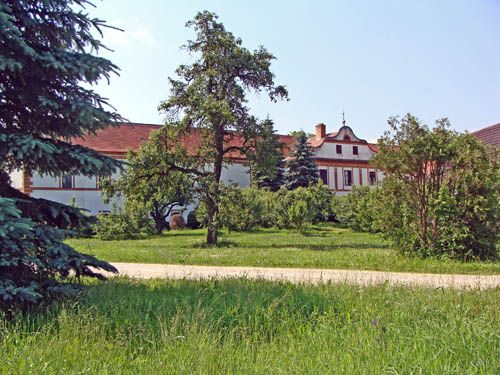 Ein historisches Gebäude mit rotem Dach, umgeben von Bäumen und grüner Wiese.