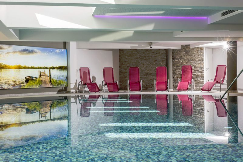 Hallenbad mit roten Liegestühlen, Steinwänden und einem großen Wandbild.