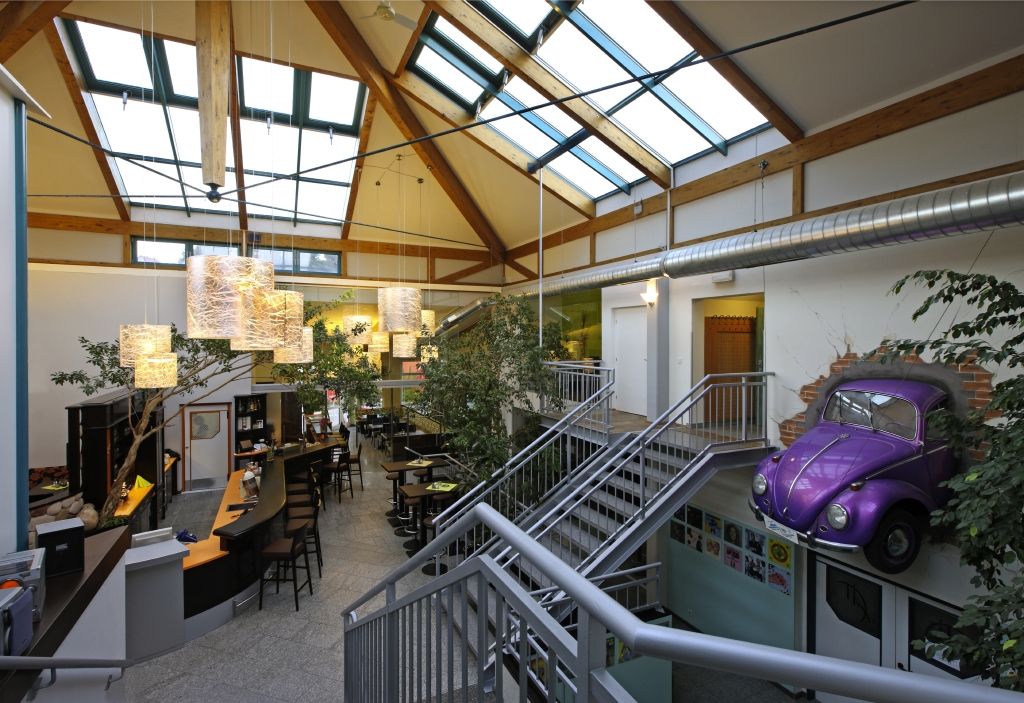 Innenansicht eines modernen Fitnesscenters mit Glasdach, Barbereich und lila VW Käfer an der Wand.