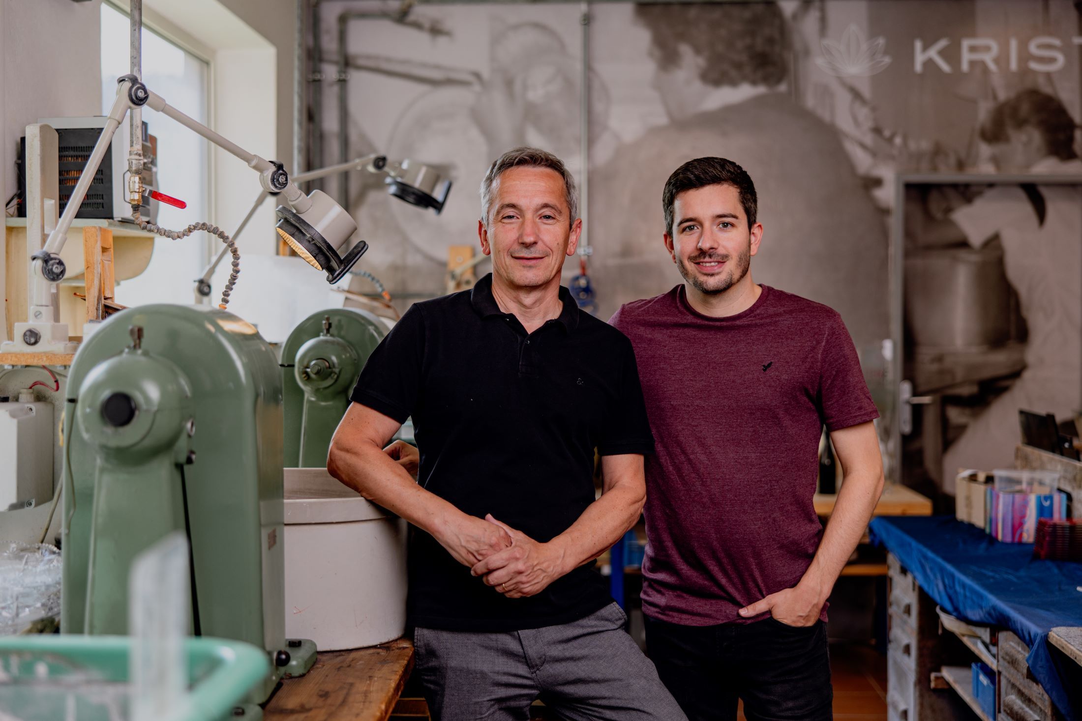 Zwei Männer stehen in einer Werkstatt mit Maschinen im Hintergrund.