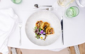 Ein Teller mit gefüllter Erdäpfelroulade und Salat auf einem gedeckten Tisch.