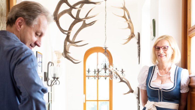 Ein Mann und eine Frau in traditioneller Kleidung stehen in einem Flur mit Geweihen an der Wand.