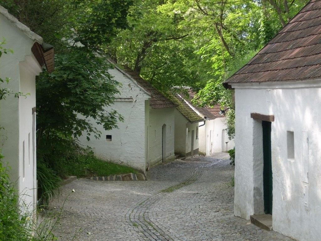 Kopfsteinpflasterstraße mit weißen Häusern und grünen Bäumen.