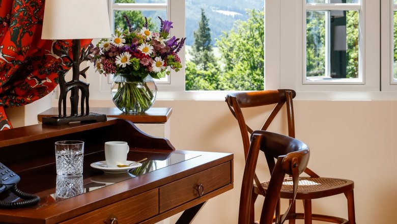 Ein elegantes Zimmer mit Holzmöbeln, einem Schreibtisch, Stühlen und einem Fenster mit Blick auf eine grüne Landschaft.