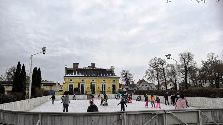 Menschen beim Eislaufen auf einem Freiluftplatz vor einem gelben Gebäude.
