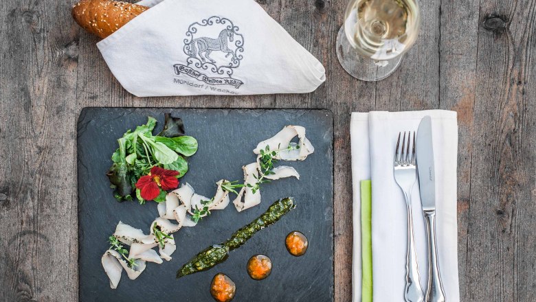 Elegante Vorspeise auf Schieferplatte mit Brot, Besteck und Weinglas auf Holztisch.
