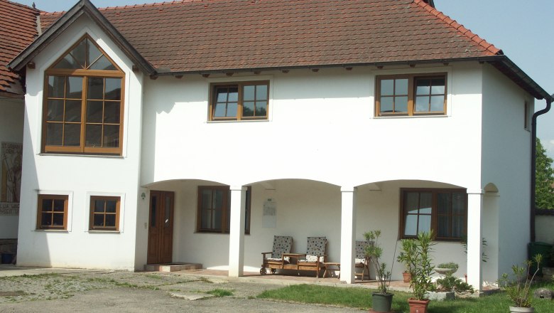 Weingut Wagner, © Fam. Wagner Ein zweistöckiges weißes Gebäude mit roten Dachziegeln und großen Fenstern. Vor dem Haus stehen Pflanzen in Töpfen.