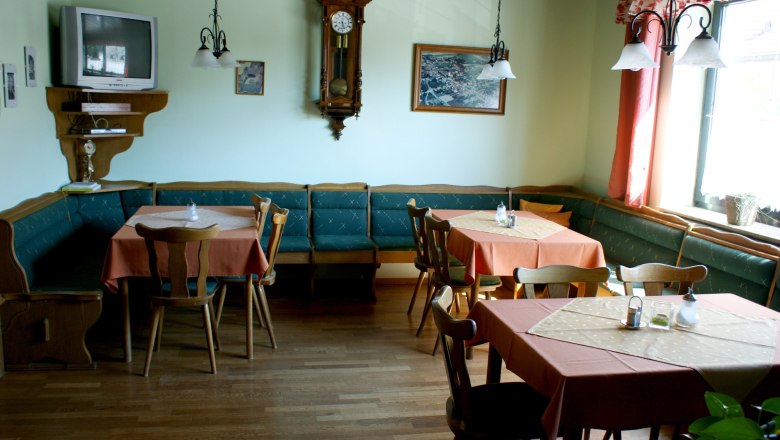 Ein traditionell eingerichteter Frühstücksraum mit Holzmöbeln, Tischen mit orangefarbenen Tischdecken, einer Wanduhr und einem Fernseher.