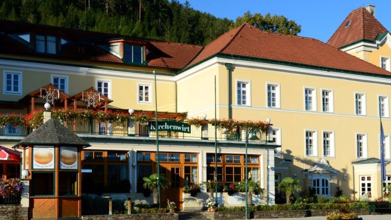 Au&szlig;enansicht eines gelben Geb&auml;udes mit roten D&auml;chern und dem Schild 'Kirchenwirt'.