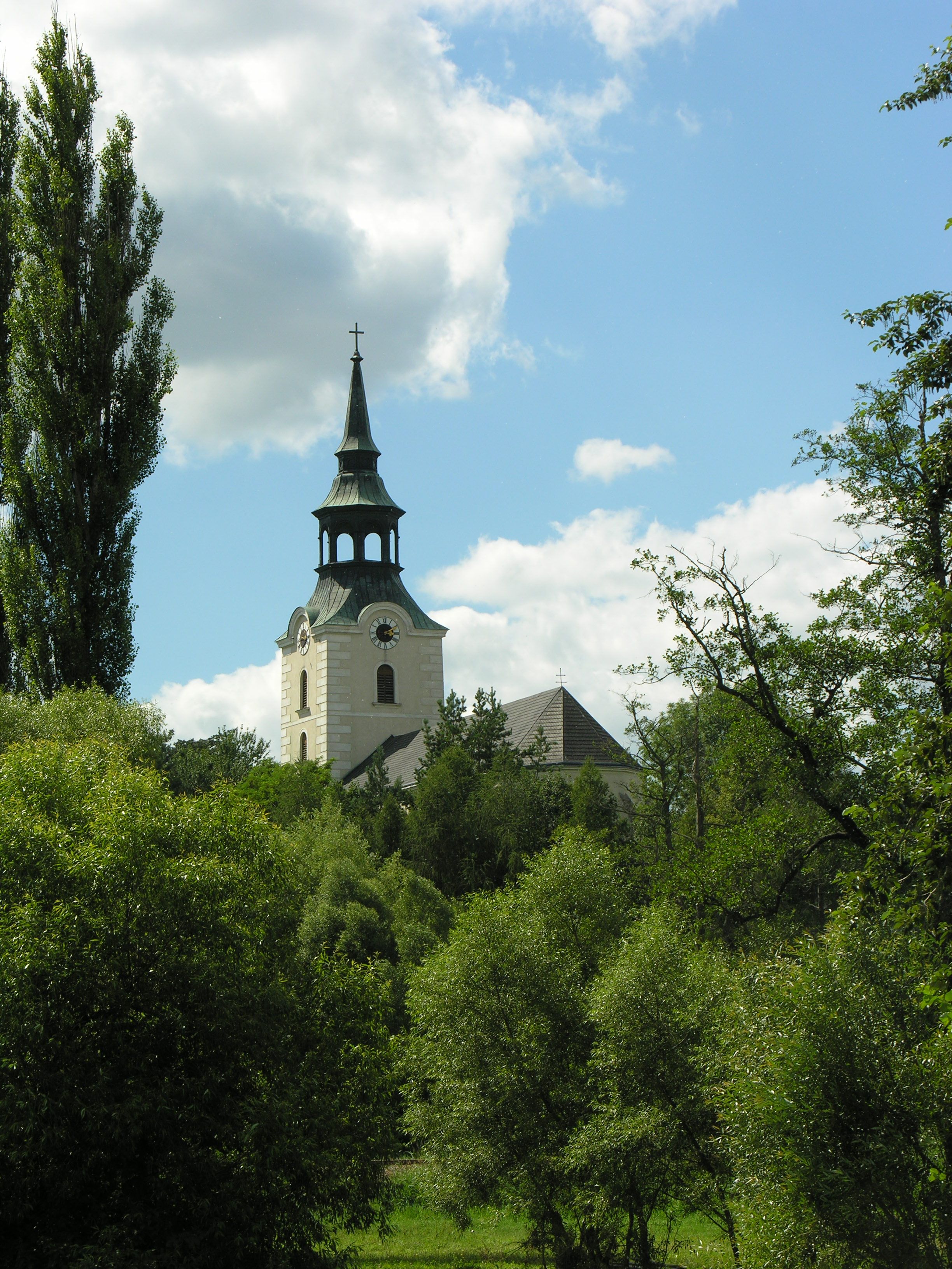 Kirchturm in Dobersberg umgeben von Bäumen und blauem Himmel.